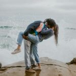 woman in blue jacket and gray pants carrying woman in blue jacket on beach during daytime