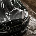 Black car covered in soap suds during wash.