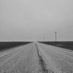 grayscale photo of road between grass field