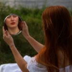 a woman sitting on a blanket looking at her reflection in a mirror