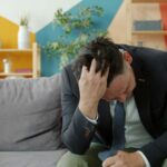 Man in suit sitting on couch with head in hands.