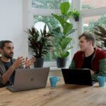 man in red and black crew neck t-shirt using silver macbook